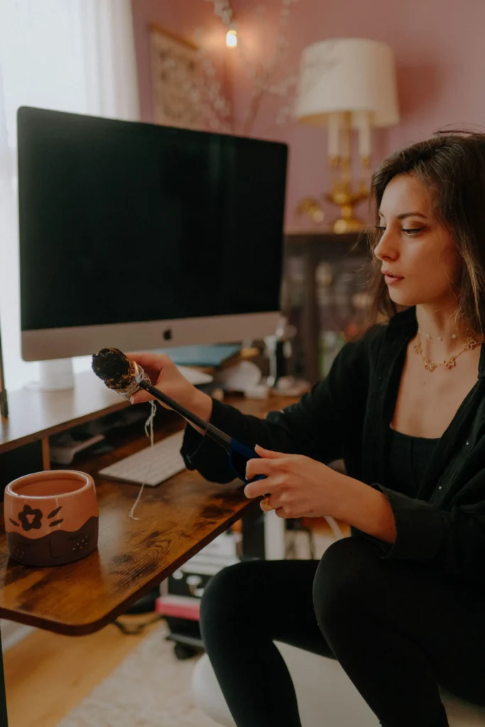 photo of a woman lighting sage in a purple home office with twinkle lights